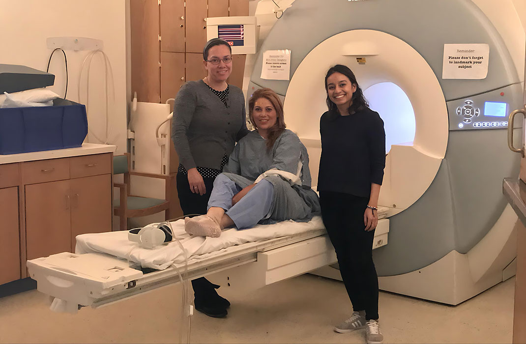 Two researchers flank a woman sitting on an MRI bed.